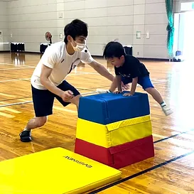 跳び箱を指導する大久保先生と跳び箱を跳ぶ年中児の男の子