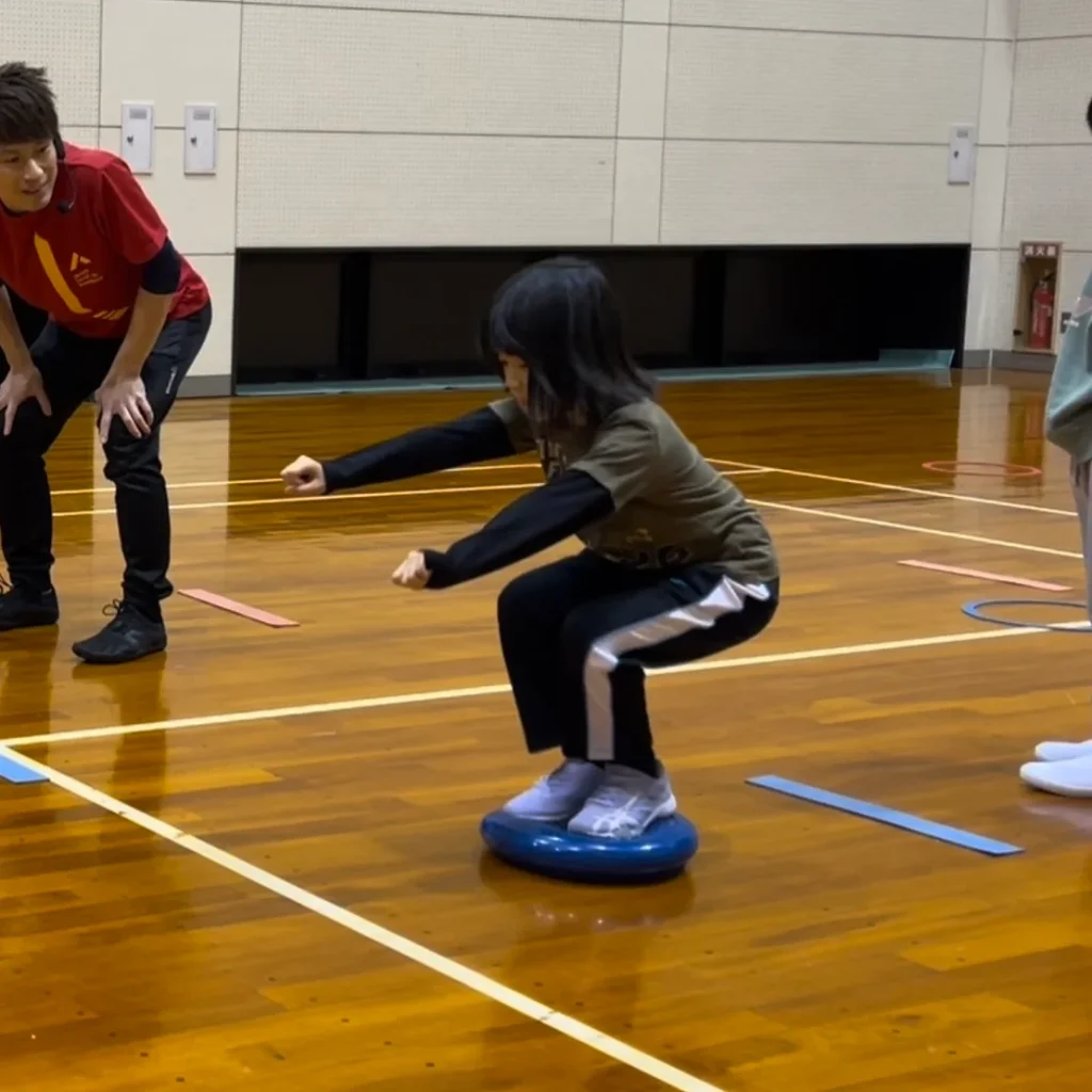 重心をコントロールする練習の為、バランスディスクに乗って腰を落とす小学生女児の子供