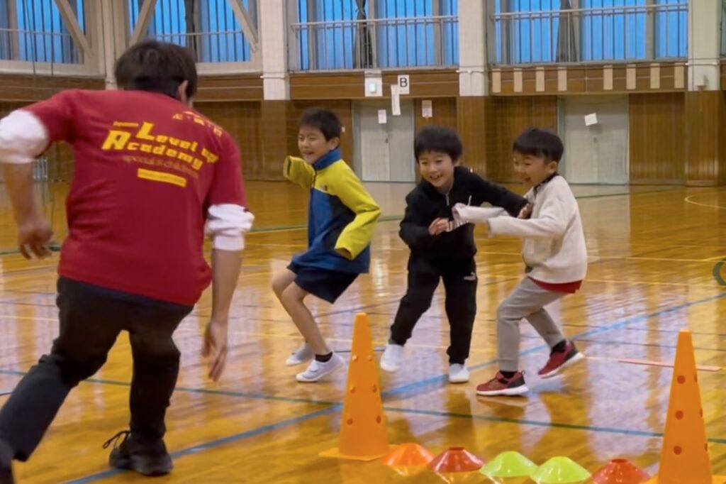 金沢市教室にて、笑顔で鬼ごっこをする幼児の男の子三人と、指導する大久保先生