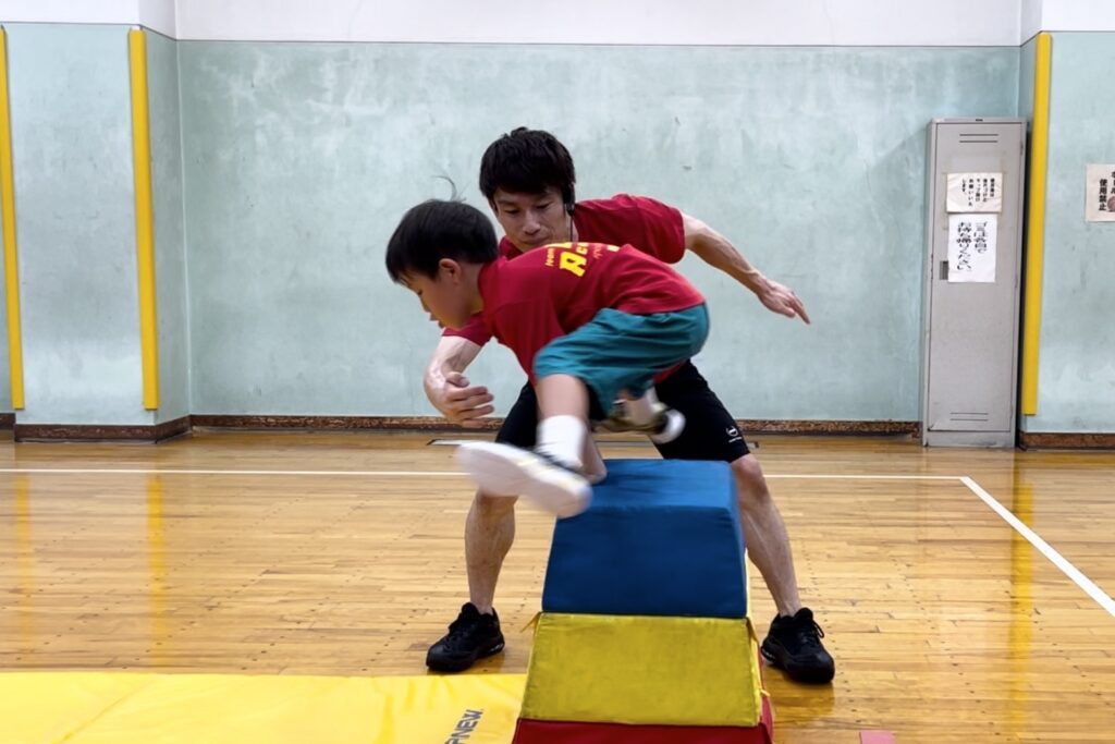 野々市市教室にて、跳び箱をカッコよくとぶ小学生男児の子供と、サポートする大久保先生