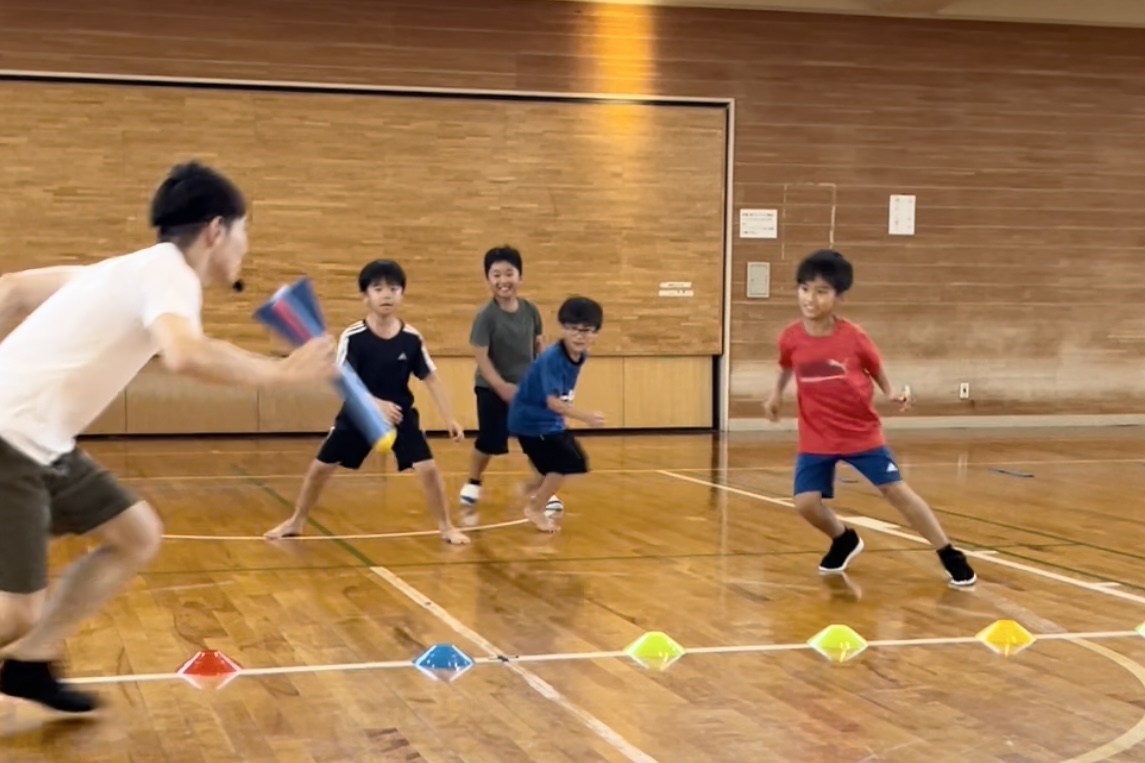 福井市教室にて、楽しそうに鬼ごっこをする小学生の男児の子供四人と指導する大久保先生