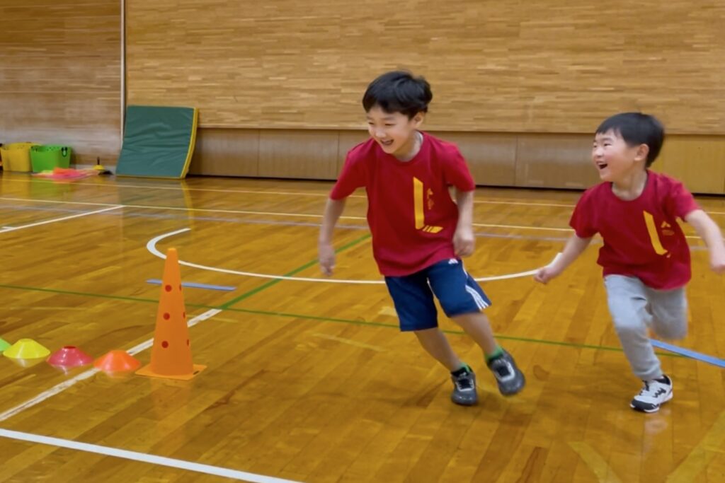 福井市教室にて、満遍の笑顔で鬼ごっこをする幼児の男の子二人