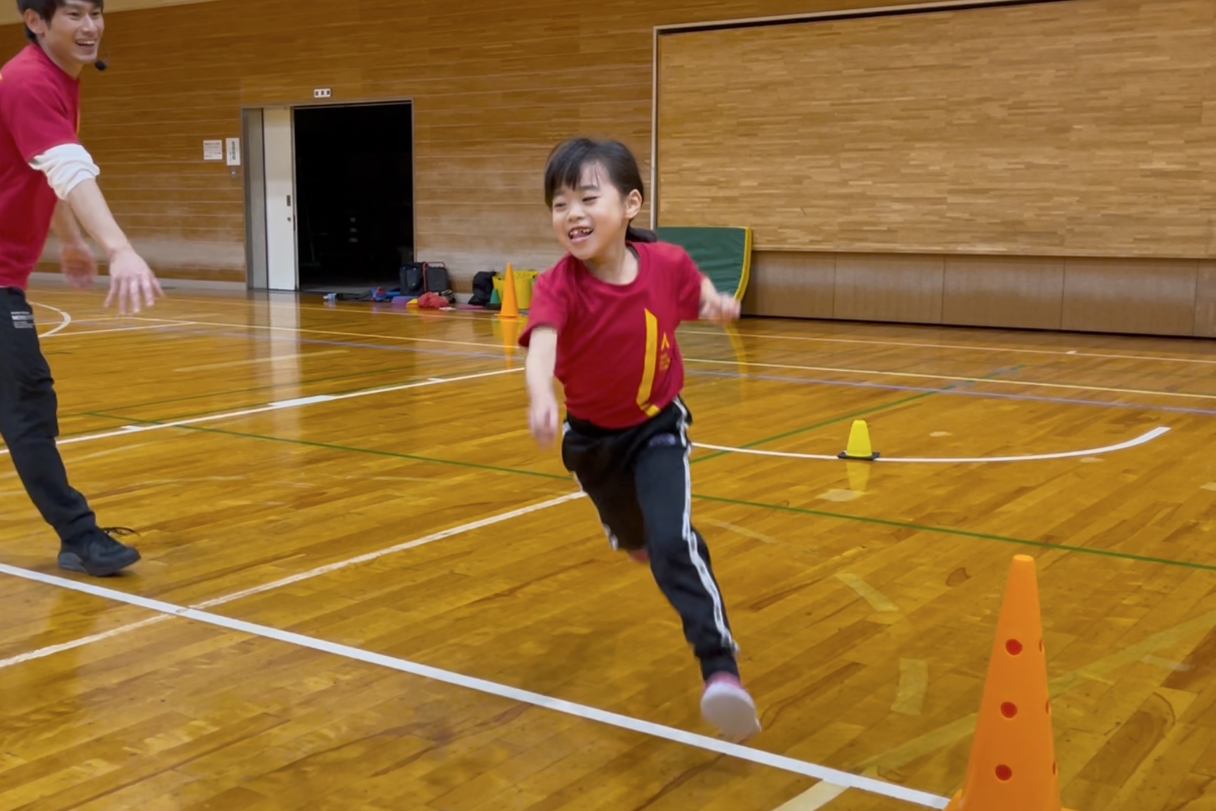 福井市教室の、オリジナルの運動神経トレーニング「先生をよけろ」にて、楽しそうにダッシュをする低学年の子供と、運動指導する大久保先生